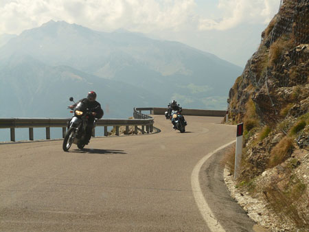 A pair of motorcyclists ride along a steep mountainside road.