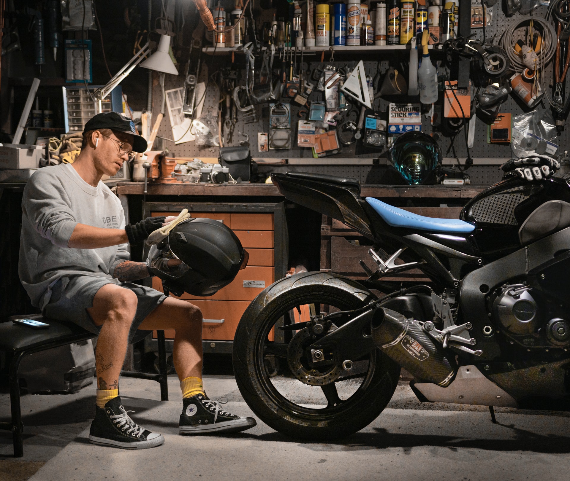 Man in grey sweater and shorts cleaning his helmet near his motorcycle