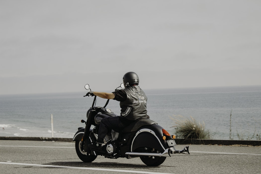 A man dressed in black riding a black motorcycle down the road.