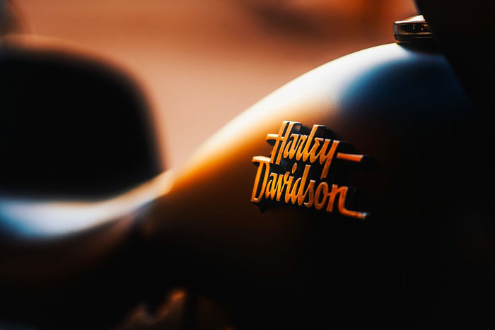 The Harley-Davidson logo, seen at an angle on the side of a motorcycle with dramatic backlighting.