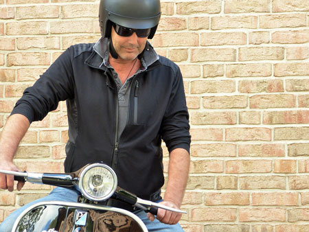 A motorcyclist in jeans and a zip-up wears a black Honda motorcycle helmet for protection.