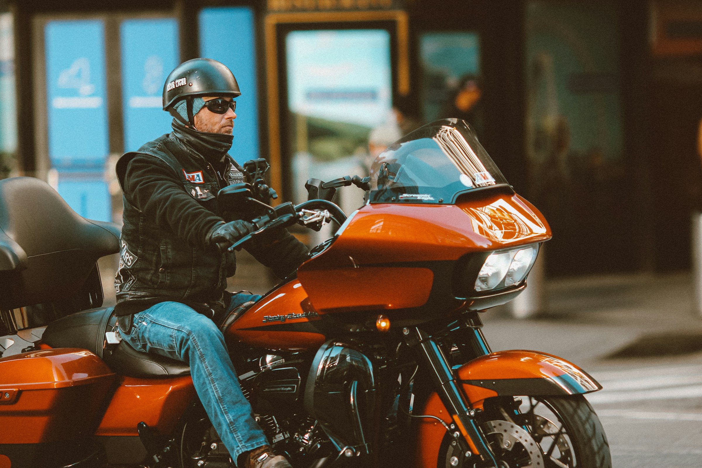 Man in a black leather jacket and blue jeans riding a motorcycle