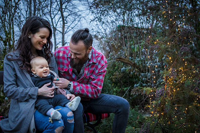 a motorcycle dad smiles at the baby in mom’s arms