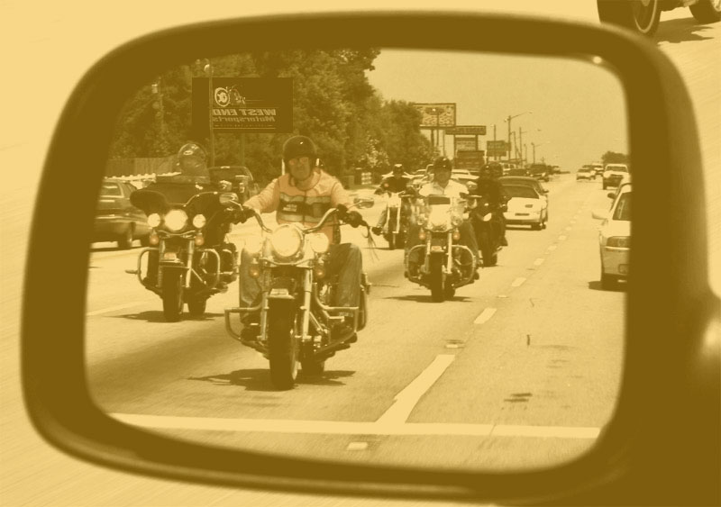 A phalanx of motorcyclists riding together on the road, as seen through a rear view mirror.
