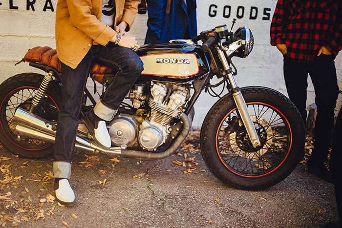 A man sits on a small Honda cruiser bike while friends stand around