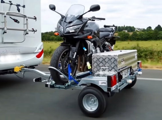 A motorcycle secured to a trailer is towed behind an RV.
