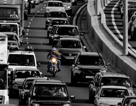 A motorcycle passes between congested lanes of cars during a traffic jam on the freeway.
