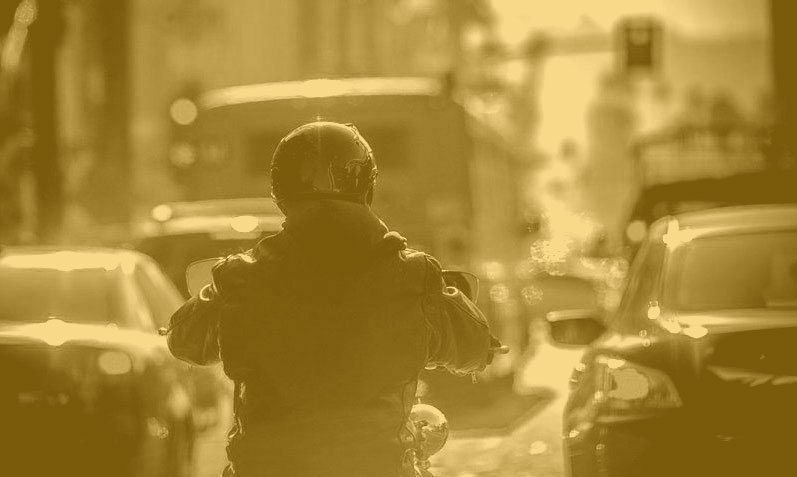 A motorcyclist, seen from behind, rides through traffic in the city.